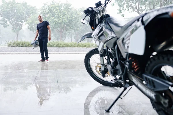 Happy smiling man with helmet in hand looking at his opened garage with motorcycle