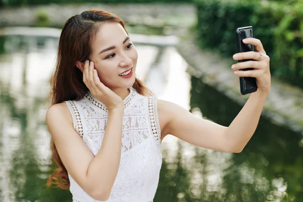 年轻美丽的亚洲女人站在城市公园的池塘边 在智能手机上拍照 — 图库照片