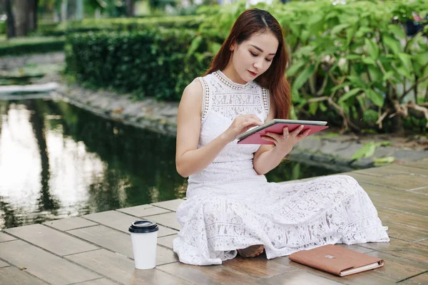 若いベトナムの大学生は コーヒーを飲みながら公園に座ってタブレットコンピュータ上でアプリケーションを使用しています — ストック写真