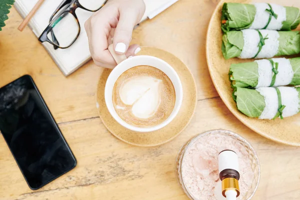 Ruka Ženy Šálkem Cappuccino Jíst Jarní Závitky Při Práci Novém — Stock fotografie