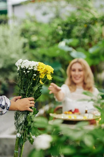 Ogrodnik Przynosząc Bukiet Kwiatów Młodej Uśmiechniętej Kobiecie Wyciągającej Ramiona Niemu — Zdjęcie stockowe