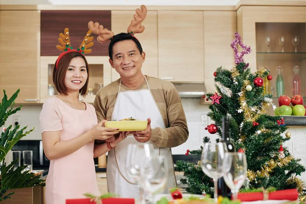 幸せな笑顔成熟したアジアのカップルを身に着けているトナカイアントラーときクリスマスディナーのテーブルを提供 — ストック写真