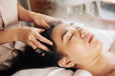 Genç Vietnamlı kadın spa salonunda dinleniyor ve kafa masajının keyfini çıkarıyor.