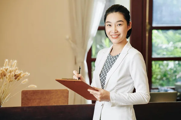 Portrait of lovely spa salon manager taking notes in document on clipboard in her hands