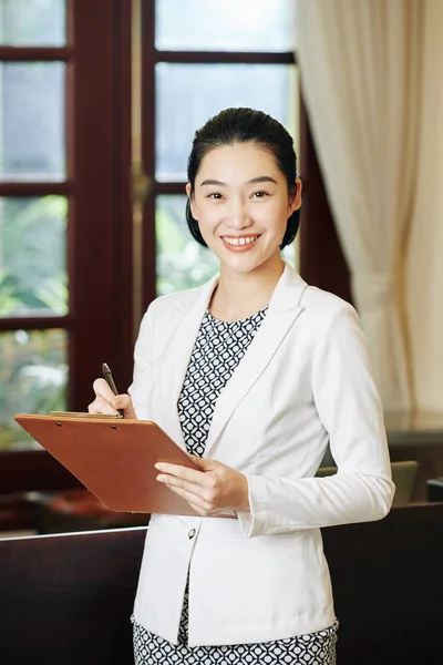 Positive pretty spa salon manager checking list of clients for the day and smiling at camera