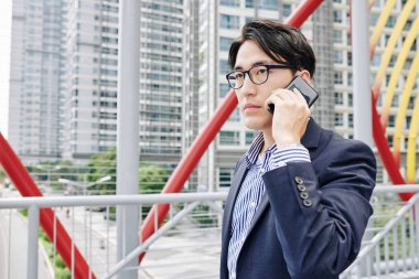 Yakışıklı, ciddi bir Asyalı girişimcinin portresi. Açık havada yürüyor ve telefonda konuşuyor.