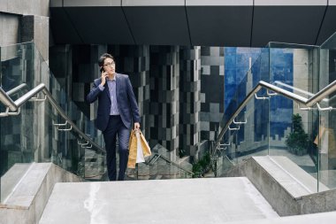 Metro istasyonundan merdivenleri çıkarken elinde kese kâğıdı taşıyan yakışıklı, kendine güvenen bir Asyalı.