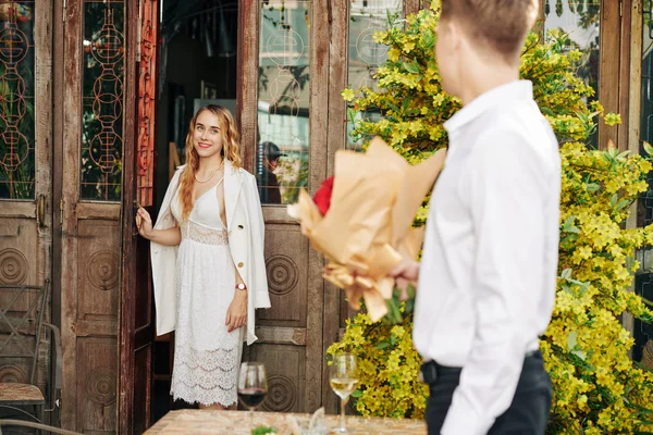 笑着年轻女人打开门 看着男朋友拿着一束鲜花等着她 — 图库照片