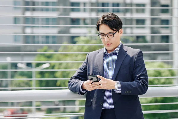 アジアの起業家が屋外に立って同僚からのテキストメッセージをチェックすることを確信する — ストック写真