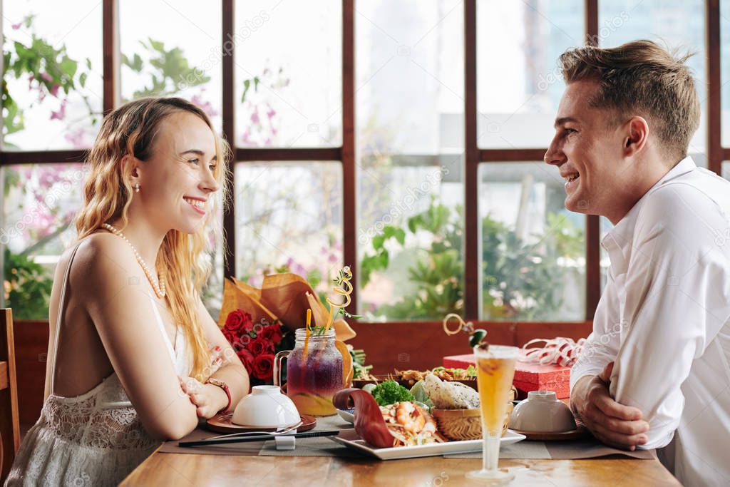 Cheerful young Caucasian couple spending first date in cafe and enjoying delicious food and conversation