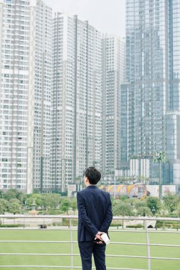 Düşünceli iş adamı elinde kahve fincanıyla yeni bölgedeki yüksek binalara bakıyor ve geleceği düşünüyor.