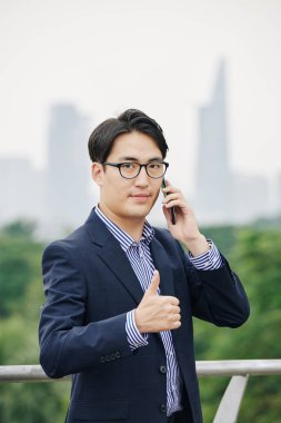 İş arkadaşıyla telefonda konuşurken gülümseyen Asyalı işadamı başparmağını kaldırdı