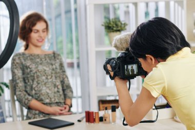 Kadın fotograf, genç bir kadının yeni makyajıyla güzellik salonunda otururken fotoğrafını çekiyor.