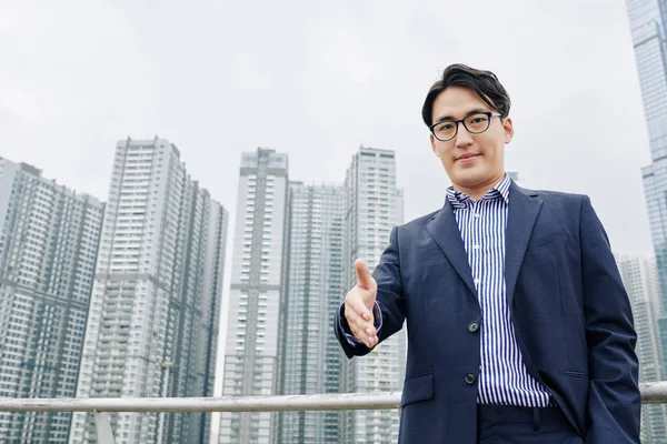 Uśmiechnięty Azjatycki Biznesmen Wyciągający Rękę Uścisk Dłoni Drapacze Chmur Tle — Zdjęcie stockowe