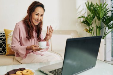 Arkadaşını selamlarken elinde bir fincan kahveyle gülen kadın onu ararken el sallıyor.