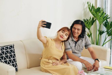 Güzel Vietnamlı bir kadın babasıyla evdeki kanepede otururken selfie çekiyor.