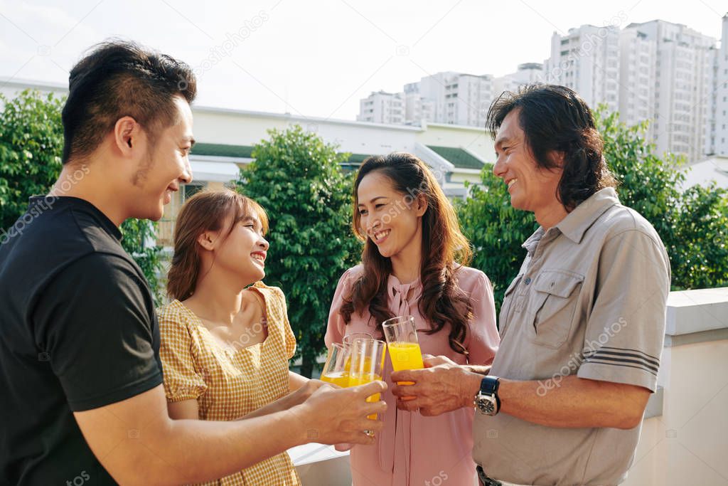 Cheerful middle-aged couple and their adult children drinking juice when having small rooftop party
