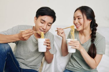 Mutlu genç Vietnamlı çift plastik bardaktan lezzetli ramen yiyor.