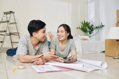 Tablet bilgisayarlı genç ve güzel Vietnamlı çift yerde yatıp apartman planlarını tartışıyorlar.