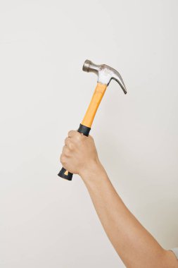 Beyaz arka planda siyah ve sarı saplı çekiç tutan tamircinin eli