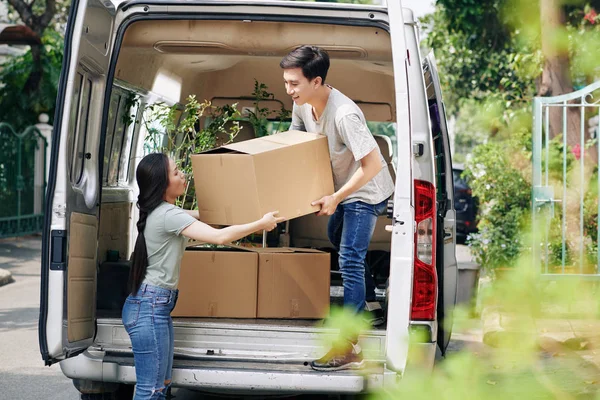 Young Asian woman helping boyfriend to take cardboard box out of car