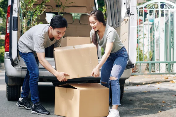 Positive Young Vietnamese Couple Taking Heavy Cardboard Boxes Out Truck — ストック写真