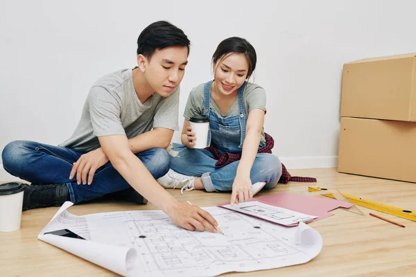 床に座って建設計画を議論する陽気な若いアジアのカップル — ストック写真