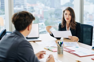 Ofis masasında oturan ve iş arkadaşıyla konuşan ciddi, genç ve güzel bir iş kadını.