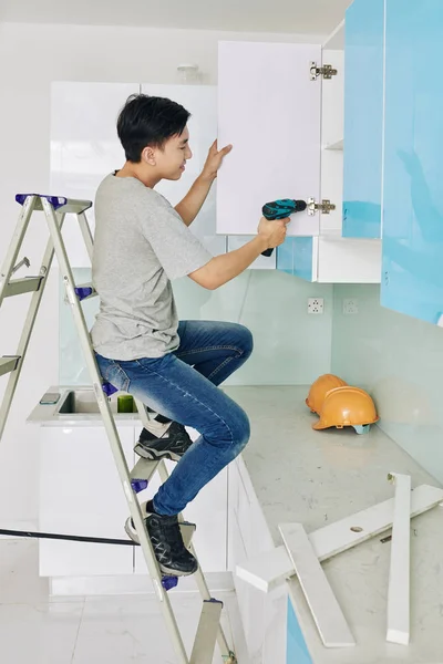 Young Asian Man Sitting Ladder Fixing Door Kitchen Cupboard — Stock Photo, Image