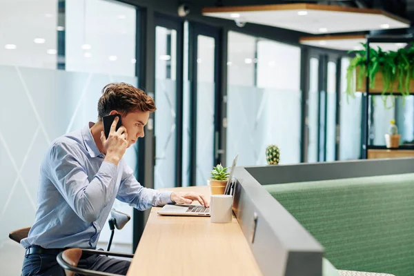 Poważny Młody Biznesmen Rozmawiający Przez Telefon Czytający Maile Ekranie Laptopa — Zdjęcie stockowe