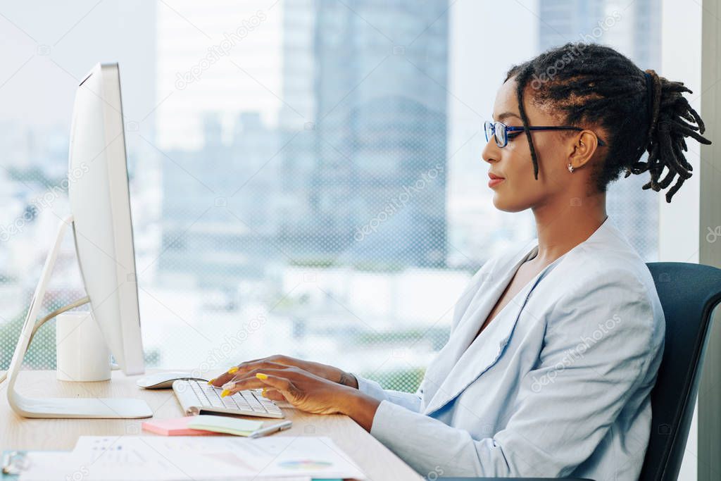 Young stylish businesswoman with dreadlocks wearing glasses when working on laptop in office