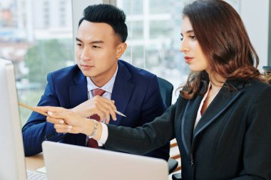 Serious multi-ethnic business executives discussing project details on computer screen at daily meeting