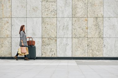 Büyük bavul ve kese kağıtlarıyla havaalanı terminaline ya da tren istasyonuna yürüyen Vietnamlı kadın.