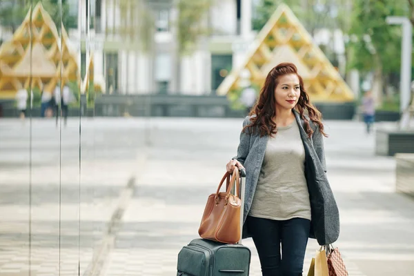 空港ターミナルに急いでスーツケースやショッピングバッグを持つかなり若い女性 — ストック写真