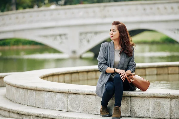 Elegant Leende Ung Kvinna Sitter Vid Fontänen Stadsparken Och Tittar — Stockfoto