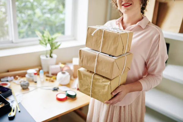 Smiling woman standing in her small home office with stack of parcels ready to be sent to customers