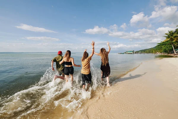 Vista Trasera Los Jóvenes Felices Emocionados Corriendo Salpicando Agua Playa —  Fotos de Stock