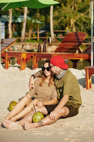 陽気な若いです男抱擁とキス彼のガールフレンドいつ彼らはビーチで休んで ココナッツ水を飲みます — ストック写真