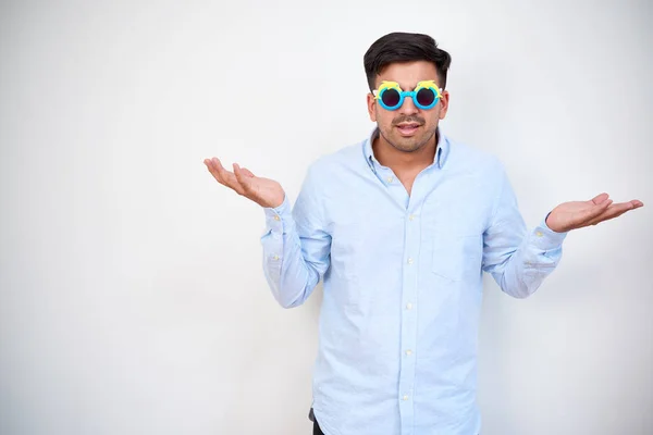Not understanding entrepreneur shrugging shoulders when standing at white wall in plastic kids sunglasses