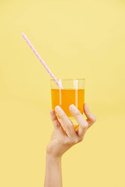 Hand of person holding glass of fresh cold orange juice with a straw