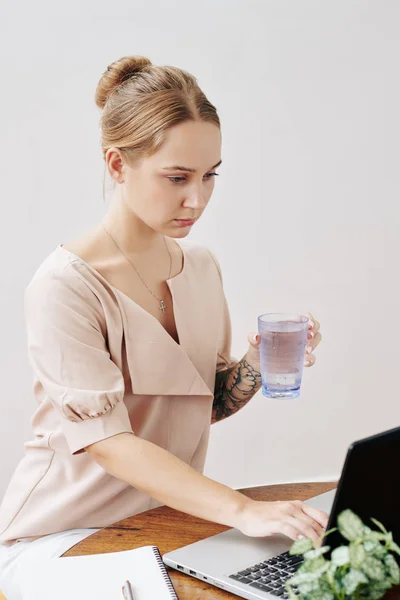 Σοβαρή Νεαρή Γυναίκα Πίνοντας Ποτήρι Γλυκό Νερό Κατά Τον Έλεγχο — Φωτογραφία Αρχείου