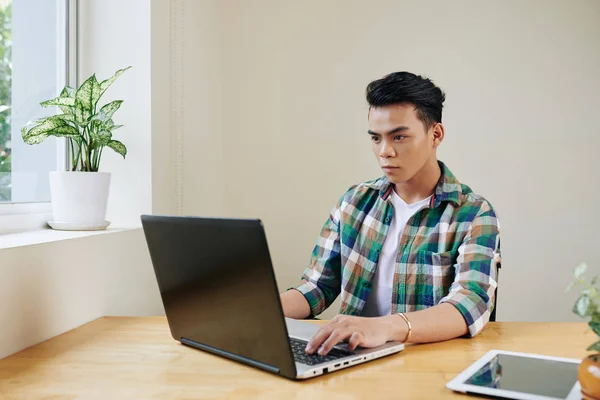 年轻的亚洲软件开发人员把精力集中在工作上 并在办公室的桌上用笔记本电脑进行编码 — 图库照片