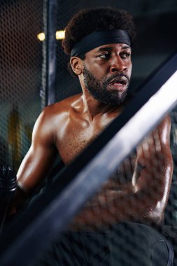 Spor salonunda üstsüz oturan yorgun Afrikalı Amerikalının dikey portresi.