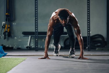 Yakışıklı genç sporcunun kameraya bakarak koşmaya hazırlandığı yatay çekim.