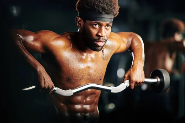 Handsome black man in sweat doing strengthening weightlifting exedrcise horizontal medium portrait