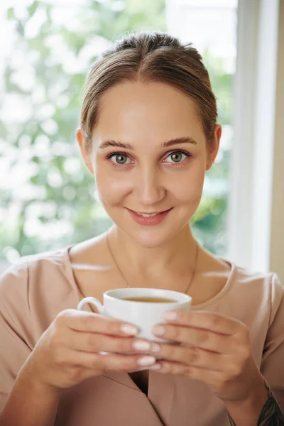 垂直中距離アップショットの魅力的な若い女性保持カップのお茶を見ますカメラ笑顔 — ストック写真