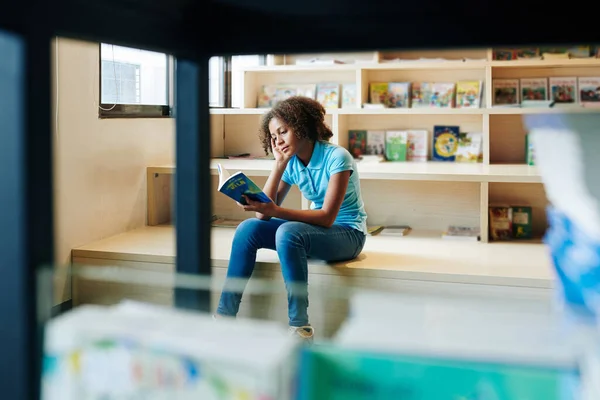 坐在图书馆看书的少女横向翻阅书架上的照片 — 图库照片