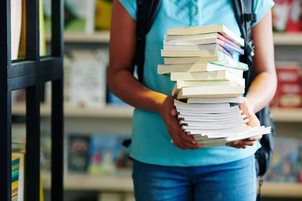 在学校图书馆的横向拍摄中 穿着蓝色衣服拿着书堆的难以辨认的少女 — 图库照片