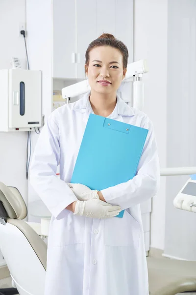 手持蓝色剪贴板 面带微笑地看着相机的美丽的亚洲女牙医的垂直中像 — 图库照片