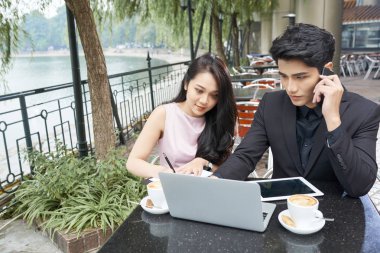 Kafe masasında yan yana oturan iki iş ortağı. Birlikte çalışan, yatay yüksek açılı bir çekim.